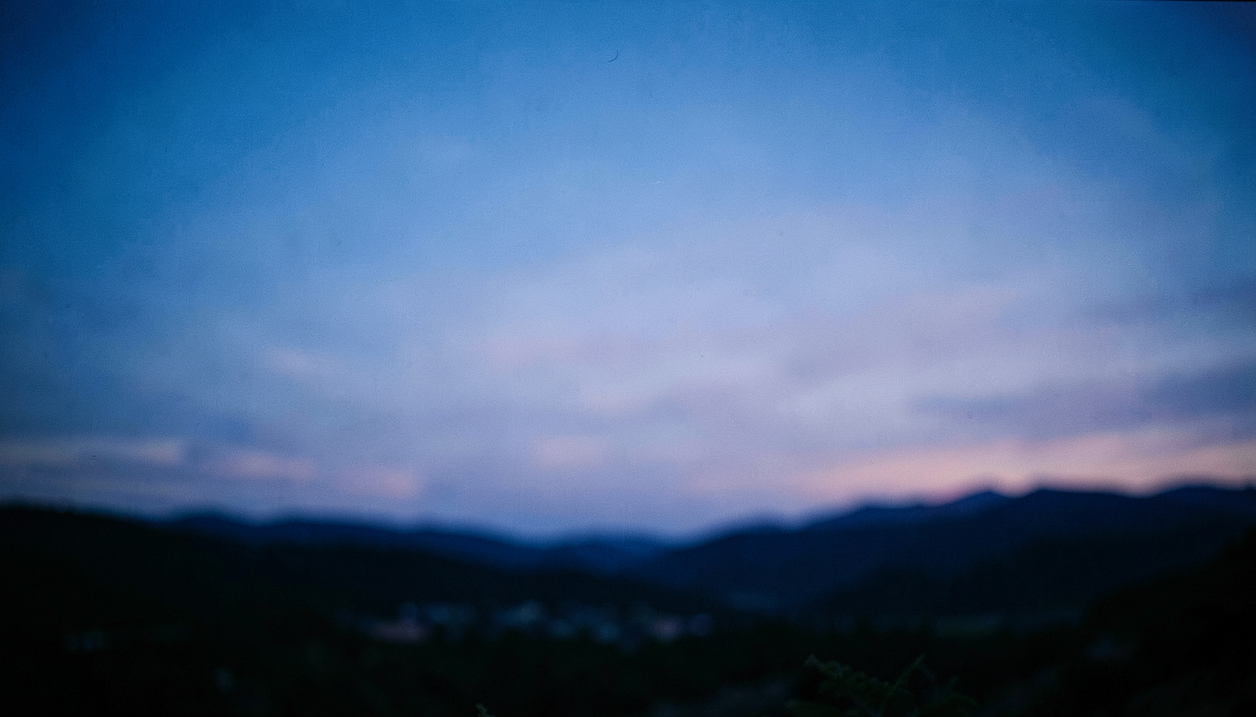 A wide cinematic frame showing a serene landscape at dusk with deep blue and soft lavender tones across the sky, shallow depth of field